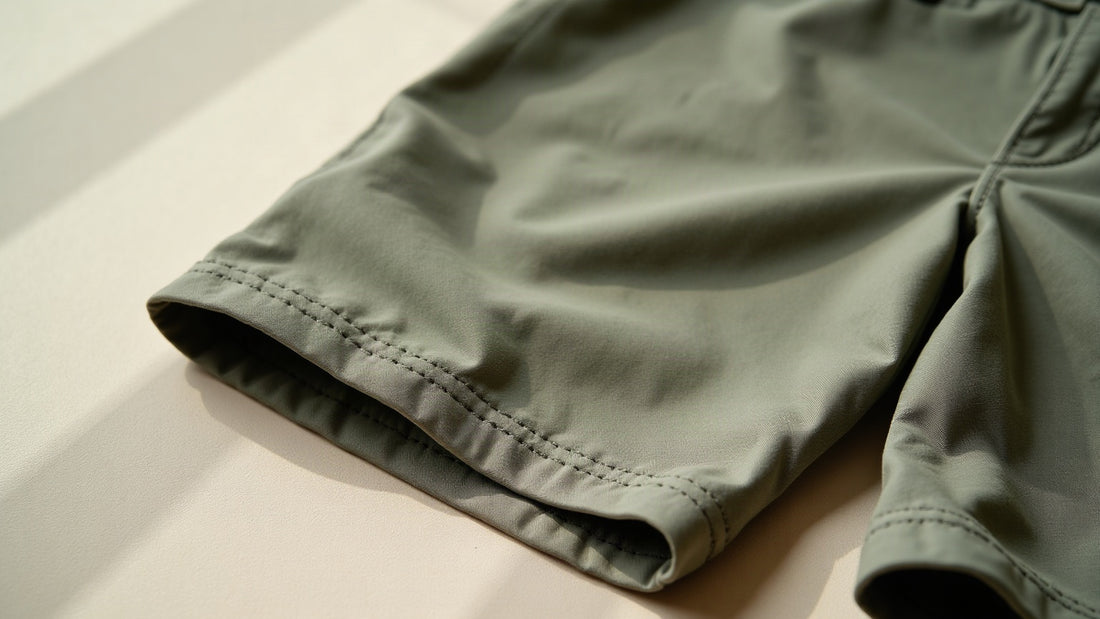 Detail of tailored men's linen Bermuda shorts in sage tone showing folded hem and waistband stitching.
