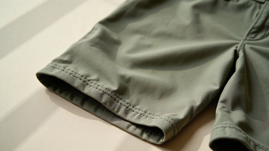 Detail of tailored men's linen Bermuda shorts in sage tone showing folded hem and waistband stitching.