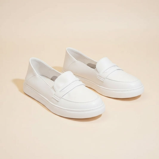 White leather penny loafers with sculpted vamp strap and tonal chunky sole, styled on a warm off-white studio backdrop.