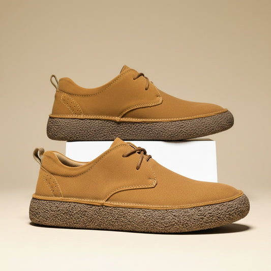 Tan suede two-eyelet derby shoes with chunky natural crepe soles and heel pull loops, styled on a warm off-white studio surface.
