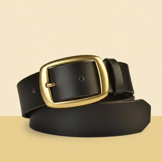 Full-grain black Italian leather belt with brushed brass rectangular pin buckle, coiled on a warm off-white studio background.