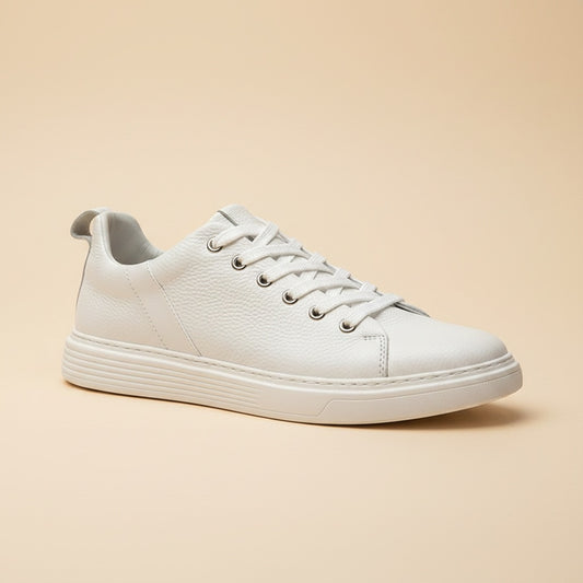 Chalk-white pebbled leather low-top court sneaker with flat laces and white cupsole, styled on warm stone in soft daylight.