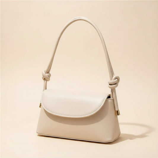 Cream leather shoulder bag with knotted top handle and curved flap on travertine ledge in soft daylight.