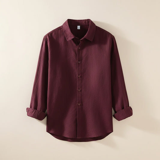 Woman in deep burgundy relaxed button-up shirt styled with ecru straight-leg trousers against a warm off-white plaster studio wall.