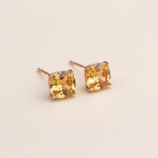 Cushion-cut citrine stud earrings in rose gold-toned four-prong settings, honey-amber facets on a warm neutral background.