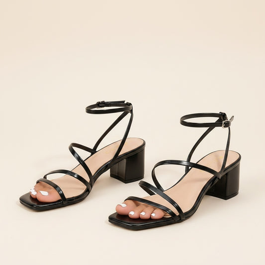 Black block-heel sandals with slim straps, ankle strap and square open toe on warm travertine in soft sunlight.