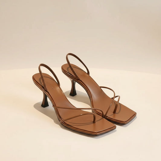 Cognac brown leather square-toe kitten heel sandals with delicate crossed straps on a warm neutral studio backdrop.