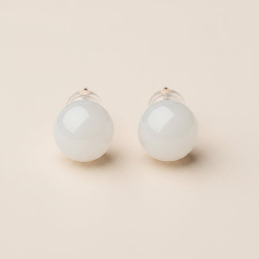 White jade orb stud earrings with slim gold posts on a warm neutral surface, softly lit in quiet-luxury minimal style.