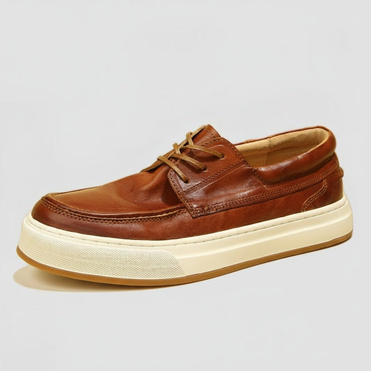 Cognac leather moc-toe deck shoe with tonal laces and cream cupsole, styled on a warm neutral ledge in soft daylight.
