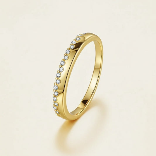 Slim gold vermeil half-eternity ring with pavé moissanite arc, softly lit on warm off-white studio surface.