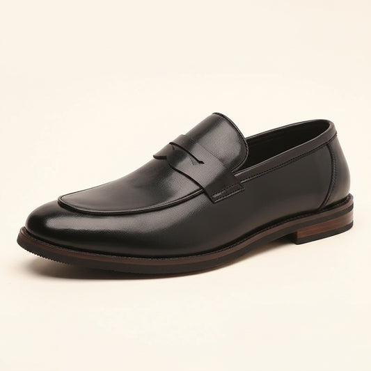 Black smooth-leather penny loafer with slim strap, almond toe and low stacked heel on a warm off-white studio surface.