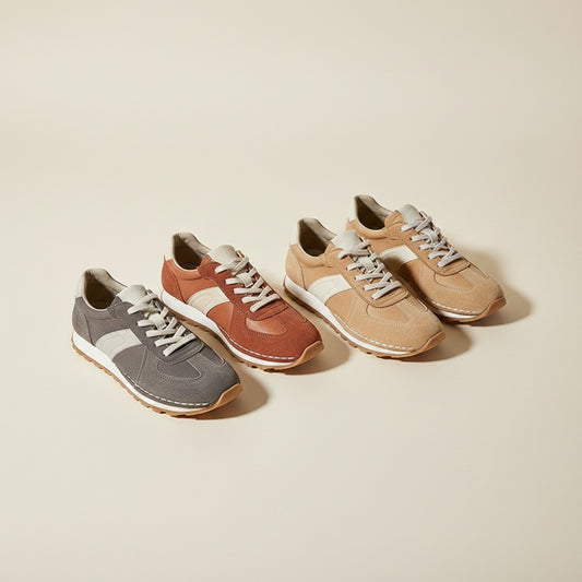 Heritage suede low-top sneakers in graphite, terracotta, and camel arranged on a stone plinth in warm off-white studio light.
