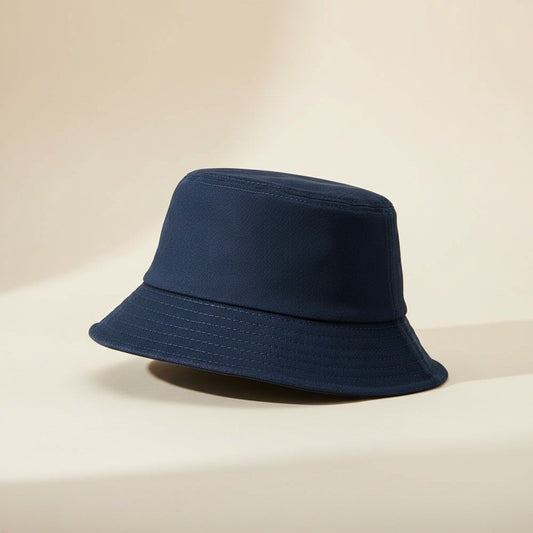 Deep navy cotton bucket hat with tonal topstitched brim, softly structured crown, styled on a warm stone surface in quiet daylight.