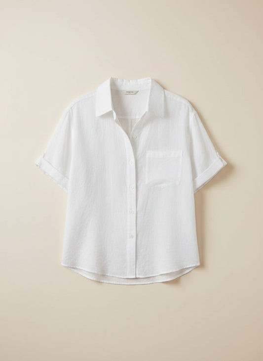 White relaxed short-sleeve shirt with spread collar and chest pocket, styled with ecru trousers in warm sunlit studio.