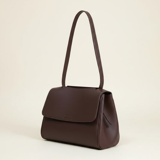 Deep burgundy structured flap shoulder bag with slim single strap, softly arched, on a warm off-white studio backdrop.