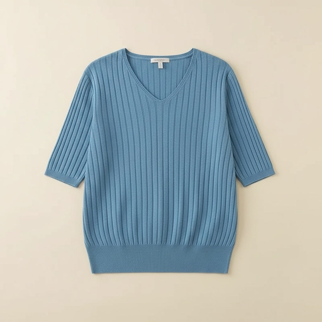 Dusty blue ribbed knit V-neck short-sleeve top styled with taupe tailored trousers against a warm plaster backdrop.