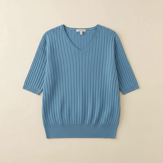 Dusty blue ribbed knit V-neck short-sleeve top styled with taupe tailored trousers against a warm plaster backdrop.