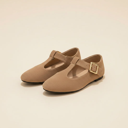 Taupe T-strap Mary Jane flats in soft suede with muted gold buckle, styled on a warm stone surface in quiet daylight.