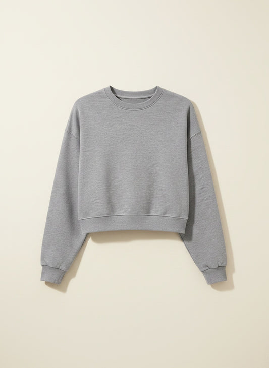 Cropped heather grey crew-neck sweatshirt styled with ecru trousers, soft daylight studio shot in quiet-luxury tones.