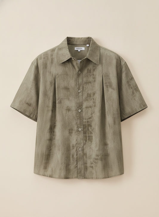 Olive shibori camp-collar short-sleeve shirt with painterly wash, styled loose over neutral trousers in soft studio light.