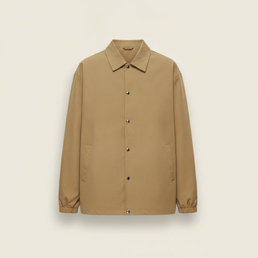 Olive shirt styled with taupe tapered trousers on a warm off-white studio backdrop, quiet-luxury editorial styling.
