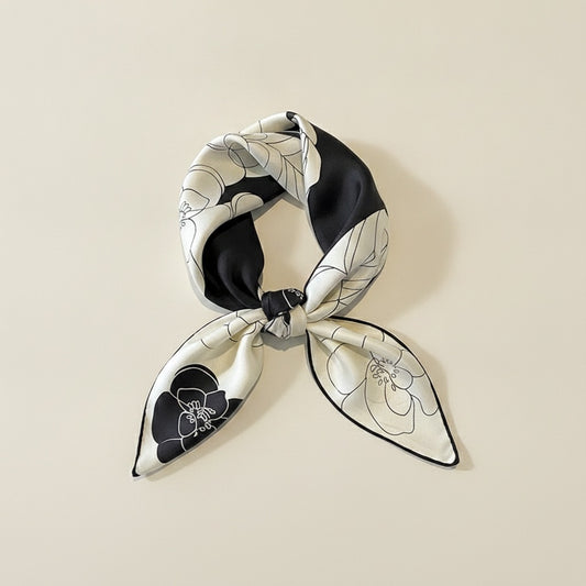 Ivory and black mulberry silk twill scarf with line-drawn floral print, softly knotted on a warm neutral studio backdrop.
