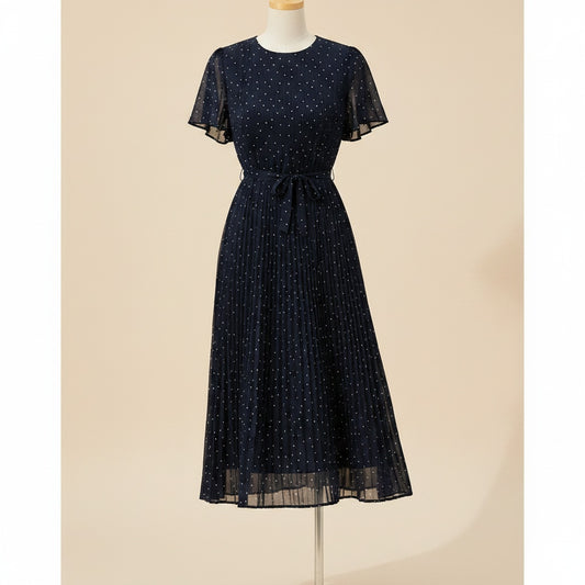 Navy chiffon midi dress with fine polka dots, flutter sleeves, tied waist and pleated skirt in soft daylight styling.