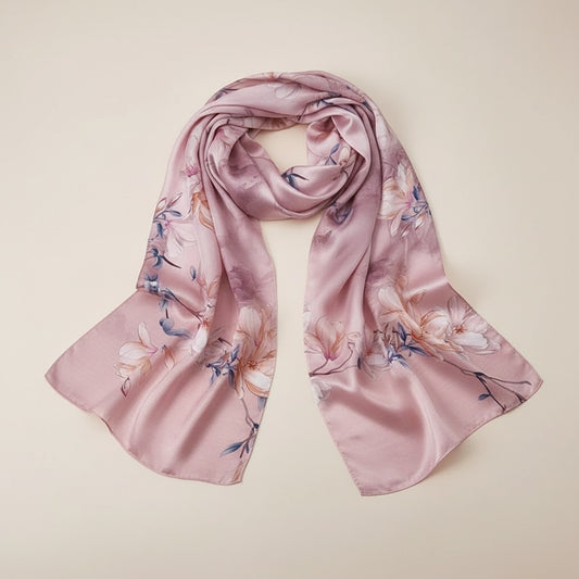 Dusty rose silk scarf with painterly magnolia blossom print, softly draped on a warm off-white studio background.