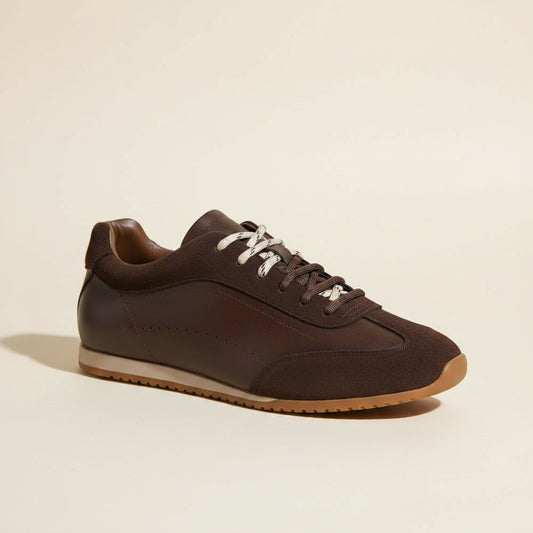 Low-profile espresso leather court sneaker with suede toe and heel panels, cream cupsole and speckled laces on warm stone.