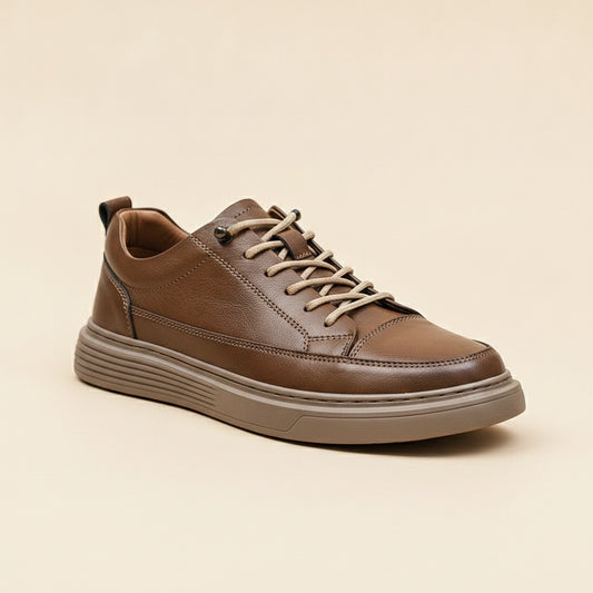 Camel brown leather low-top court sneaker with tonal stacked sole and natural laces on a warm neutral studio surface.