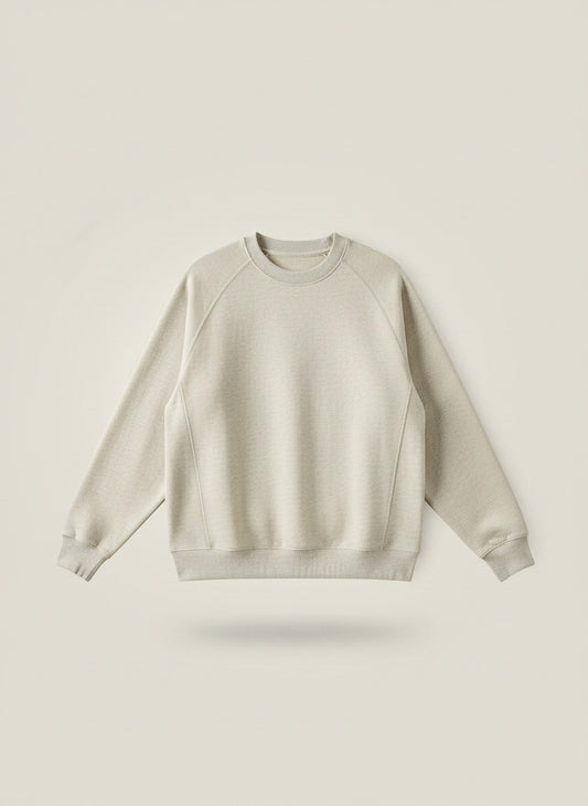 Oatmeal crewneck sweatshirt styled with tonal taupe wide-leg trousers, soft daylight against a warm off-white plaster wall.