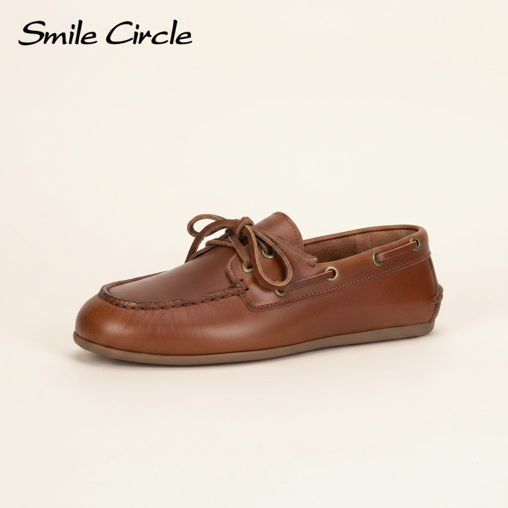 Tan leather boat moccasin with hand-stitched moc toe and brass eyelets, styled on a warm travertine surface in soft natural light.