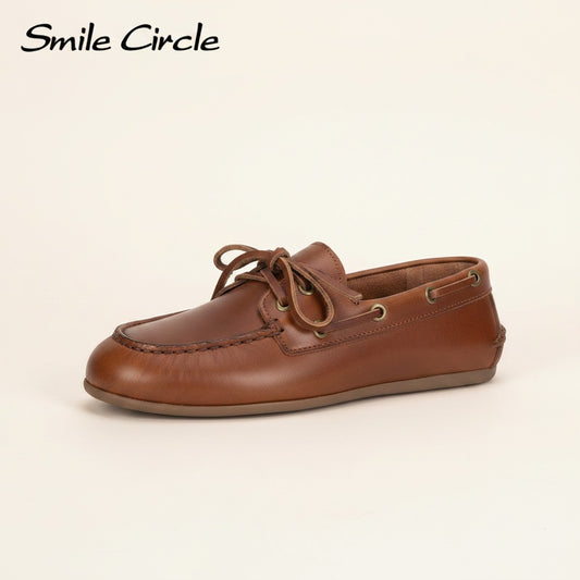 Tan leather boat moccasin with hand-stitched moc toe and brass eyelets, styled on a warm travertine surface in soft natural light.