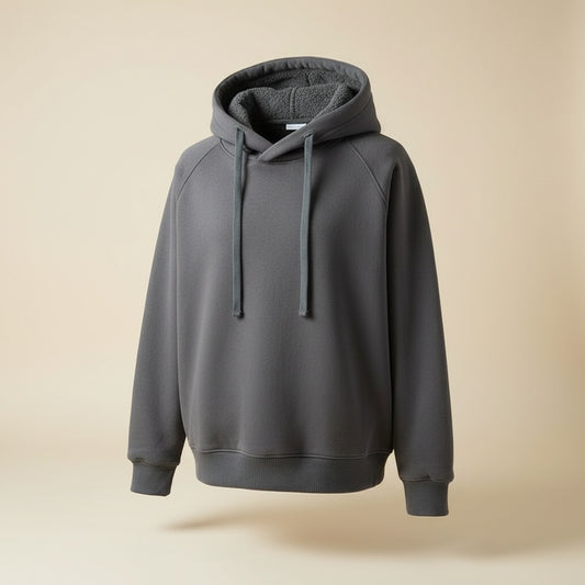 Model in iron grey hooded pullover with tonal drawcords and ribbed cuffs, styled with neutral trousers in warm studio light.