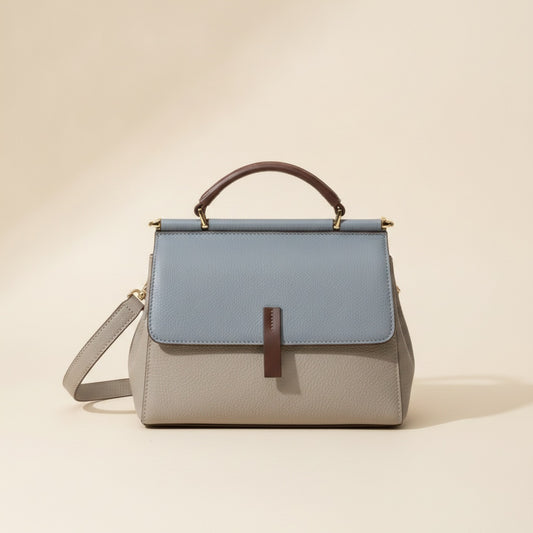 Two-tone structured leather top-handle bag in dusty blue and soft grey with vertical tab closure and gold hardware.