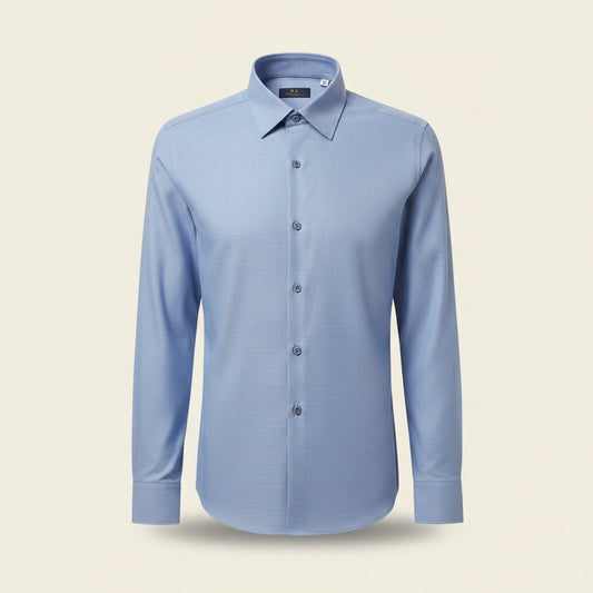 Dusty sky-blue long-sleeve shirt styled with stone tailored trousers against a warm plaster studio wall.