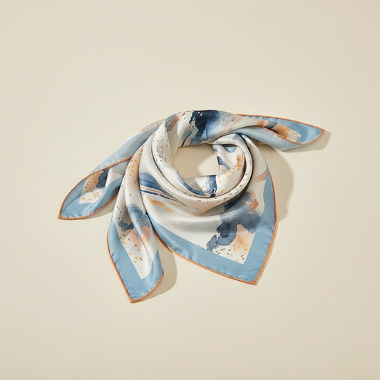Mulberry silk square scarf in ivory with watercolour blue and ochre print, hand-rolled edge, softly knotted on warm plaster.