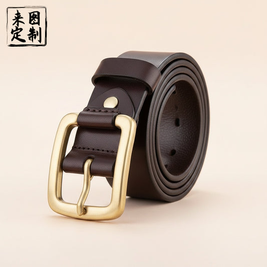 Coiled espresso full-grain leather belt with antique-brass rectangular pin buckle and tonal stitching on warm off-white studio backdrop.