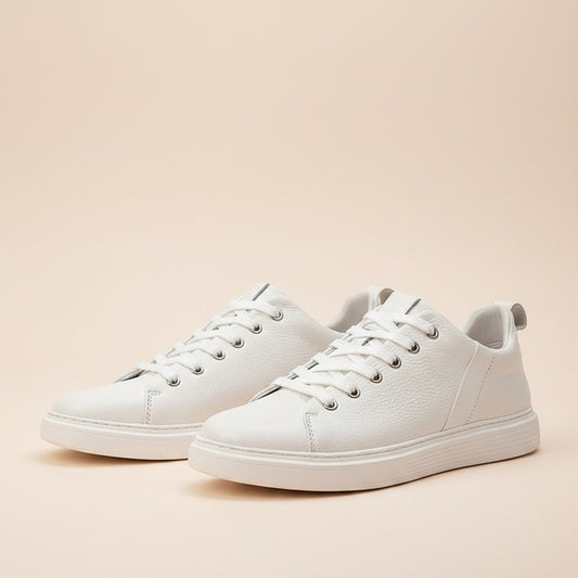 Ivory pebbled leather low-top court sneakers with tonal laces on a warm limestone ledge in soft daylight.