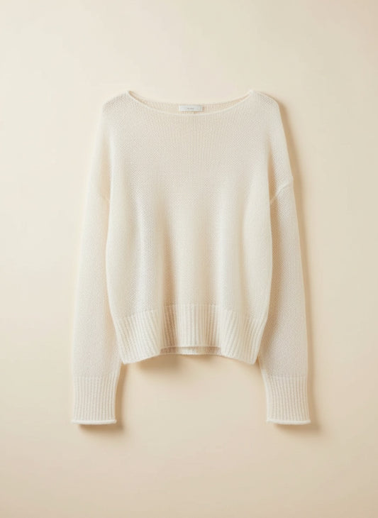 Ivory boatneck pullover styled with cream tapered trousers against a warm plaster wall in soft Mediterranean morning light.