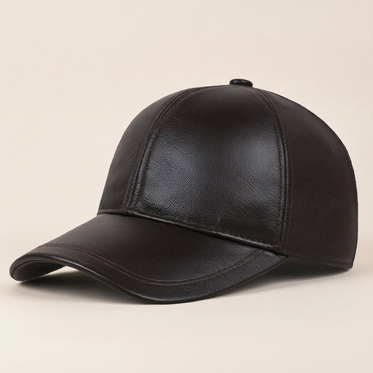 Espresso-brown leather baseball cap with curved brim and tonal stitching, styled on warm off-white linen in soft studio light.