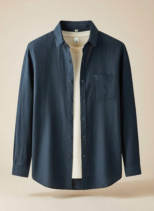 Relaxed-fit navy linen shirt worn open over a warm off-white tee with sand linen trousers, quiet-luxury coastal styling.