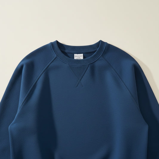Deep navy raglan-sleeve sweatshirt styled with stone tapered trousers, photographed against a warm off-white studio backdrop.