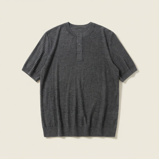 Charcoal ribbed wool short-sleeve henley knit top styled with stone tailored trousers against a warm off-white plaster wall.