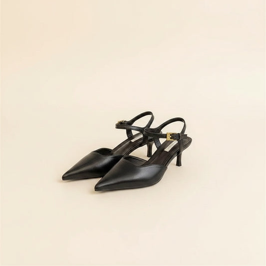 Black pointed-toe slingback kitten heels with slim ankle strap and gold buckle, styled on warm neutral studio backdrop.