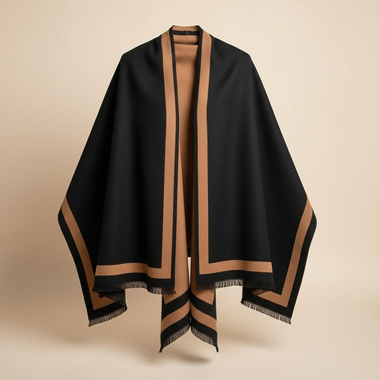 Oversized reversible wrap in black and camel with wide contrast border and softly fringed edges, draped in warm studio light.